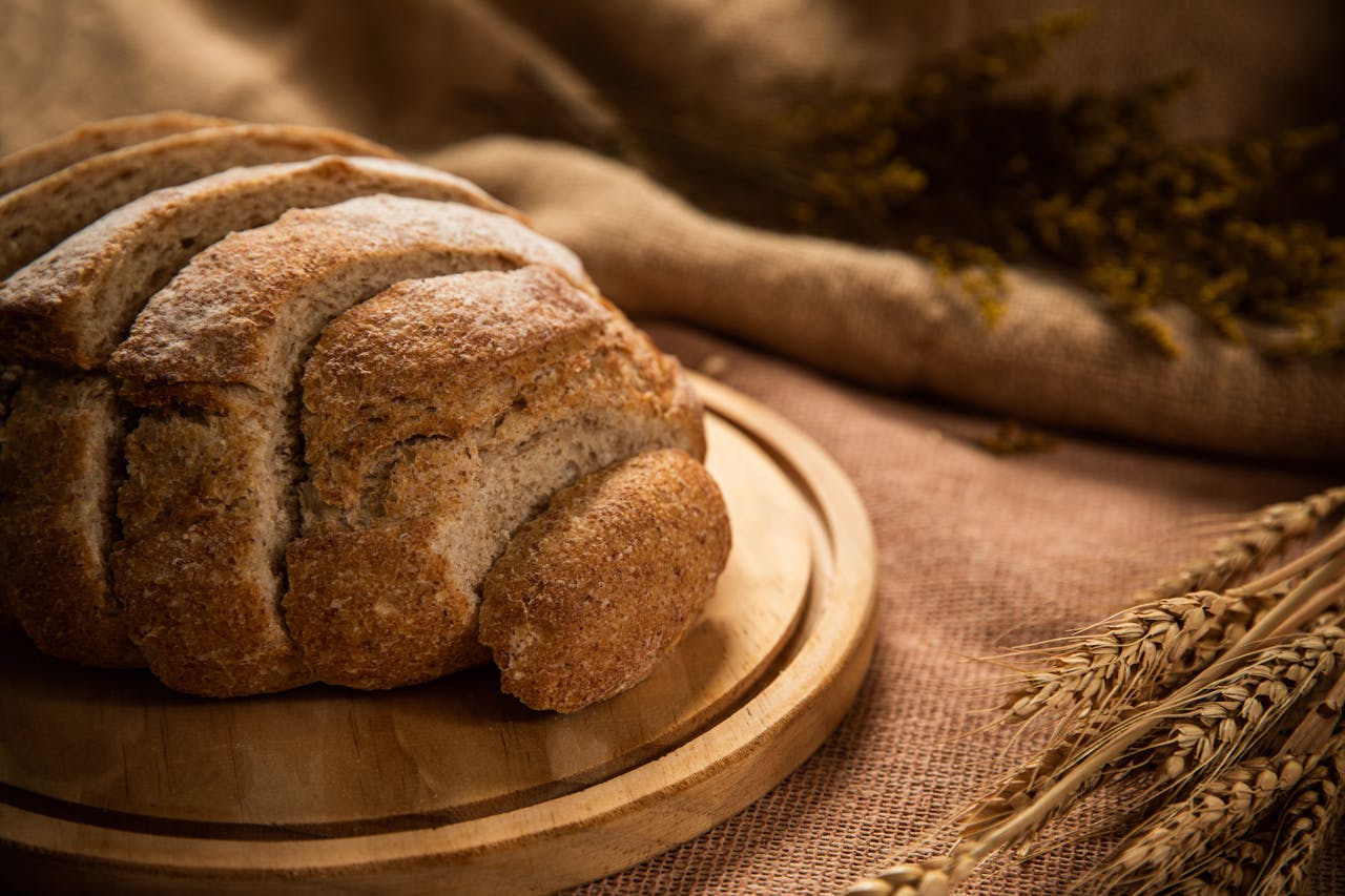 Delicious freshly baked whole wheat bread loaf on a wooden board with wheat in the background.