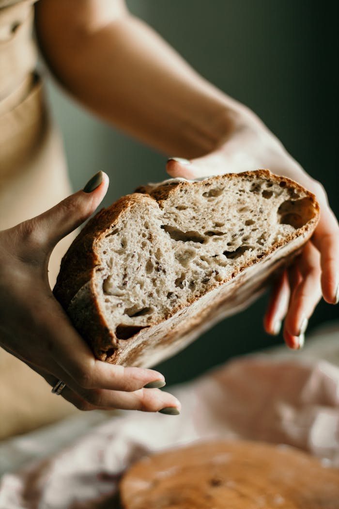Close-up of fresh sourdough bread held by baker's hands, showcasing texture and artisan quality.